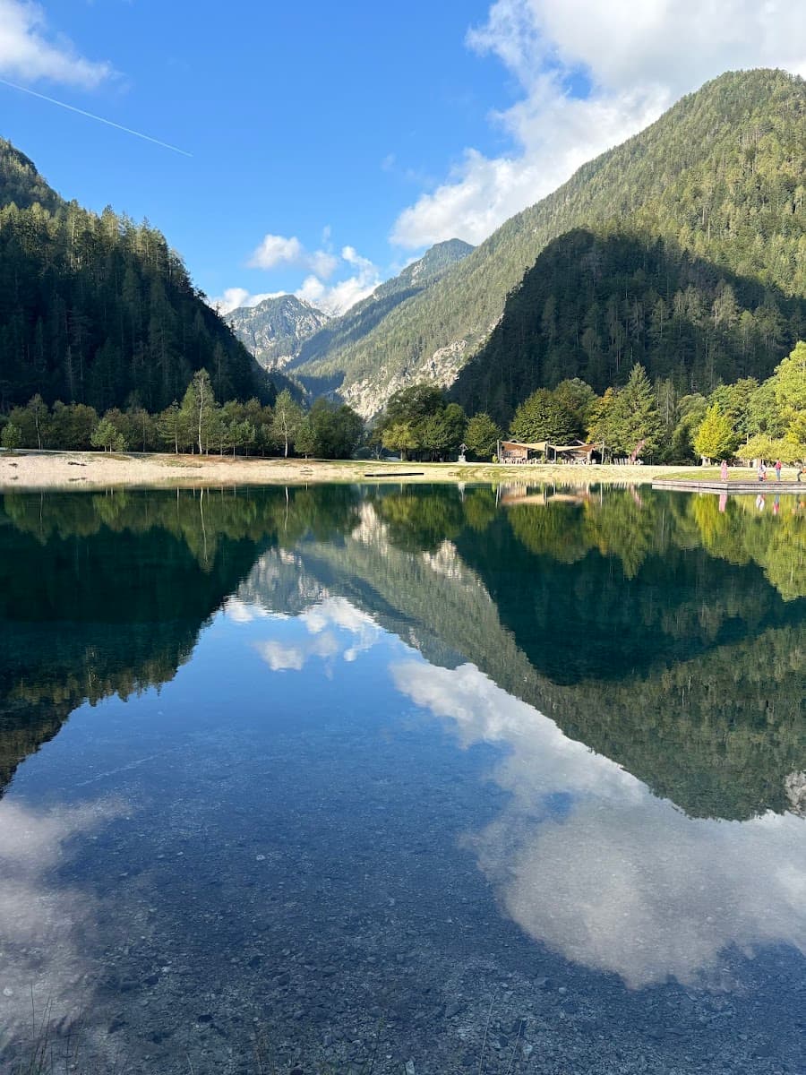 Alpine lake with clear water reflecting forested mountains under a blue sky