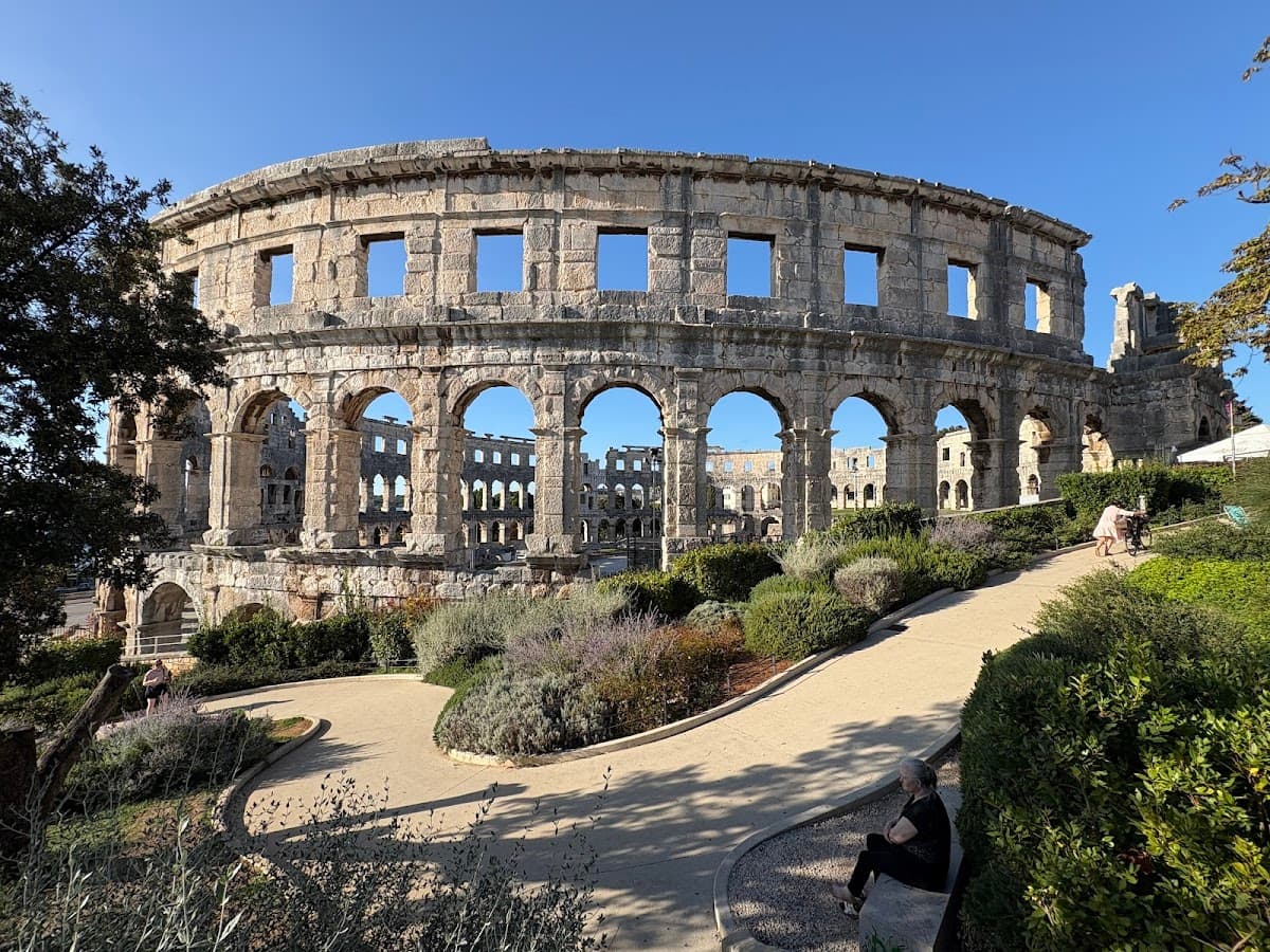 Ancient Roman amphitheater ruins with arched exterior and garden path in foreground