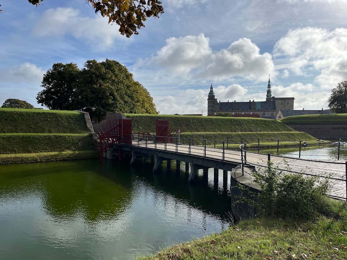 Wooden bridge over moat leading to historic fortress with grassy ramparts