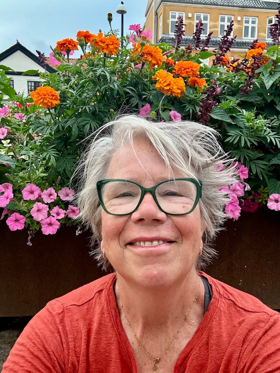 Woman with glasses smiling in front of colorful orange and pink flowers